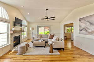 Living area featuring vaulted ceiling, light wood-style flooring, ceiling fan, and a glass covered fireplace