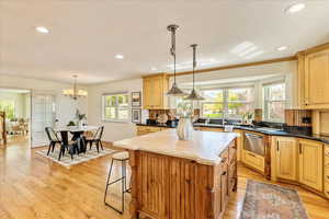 Kitchen featuring a center island, light wood-style flooring, a kitchen breakfast bar, dishwasher, and suspended lighting