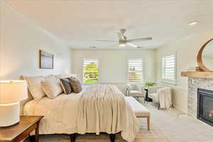 Carpeted bedroom featuring a textured ceiling, ceiling fan, a stone fireplace, and ornamental molding