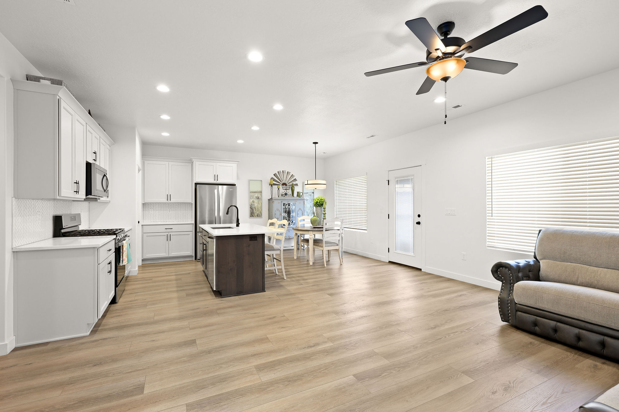 Dual tone kitchen with open floor plan, a kitchen island with sink, two tone cabinetry, stainless steel gas range oven, and light wood-type flooring