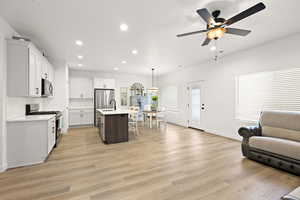 Dual tone kitchen with open floor plan, a kitchen island with sink, two tone cabinetry, stainless steel gas range oven, and light wood-type flooring