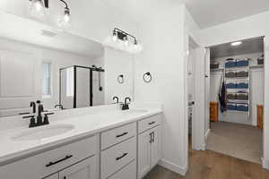 Full bathroom featuring a walk in closet, double vanity, a shower stall, and light wood-type flooring