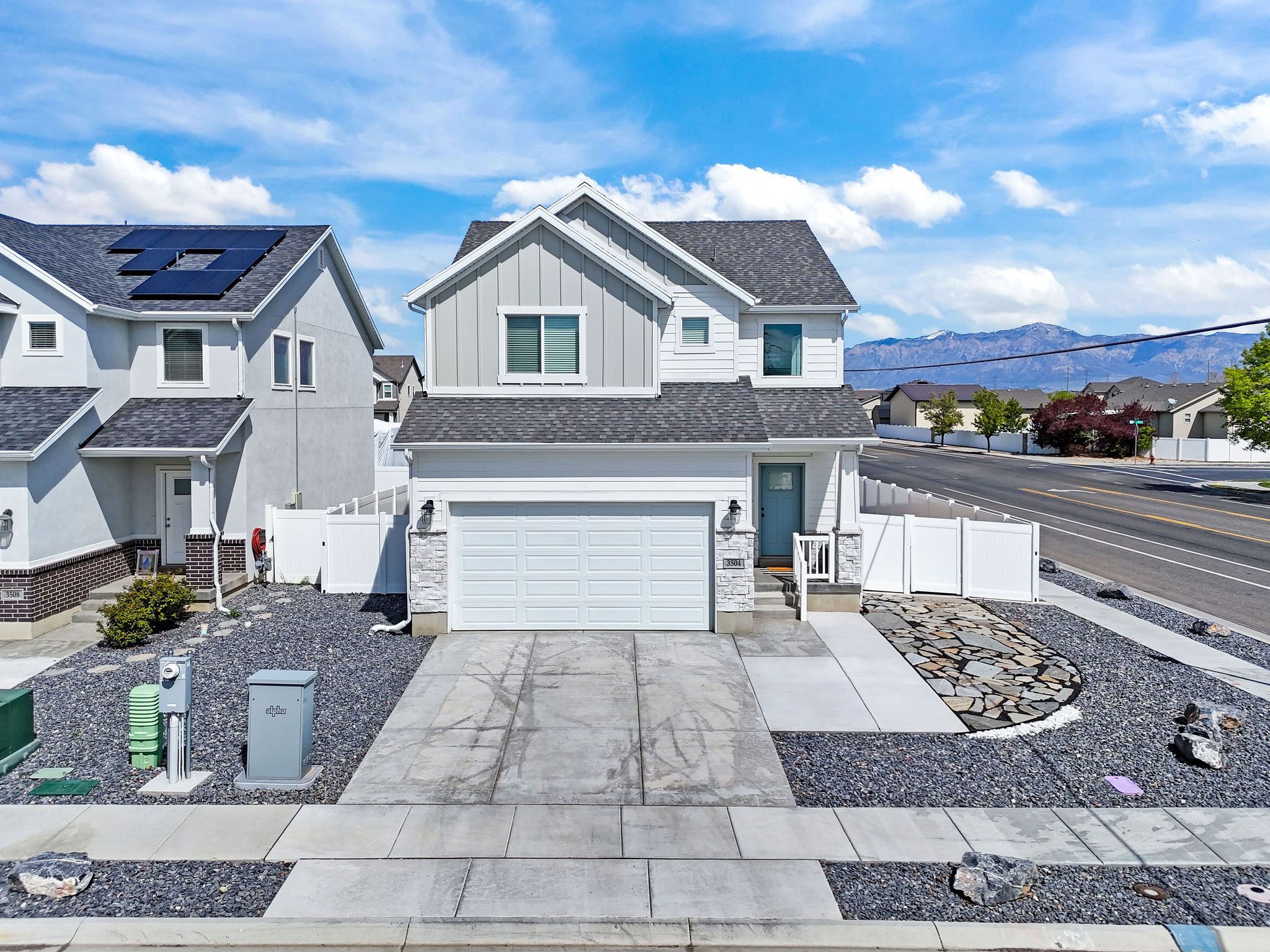 Traditional-style home with board and batten siding, a residential view, an attached garage, driveway, and a gate