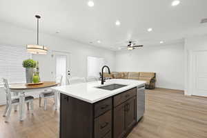 Kitchen featuring dark wood finish cabinetry, light wood-style floors, a center island with sink, and open floor plan