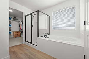Full bath with light wood-style floors, a spacious closet, a garden tub, and a stall shower