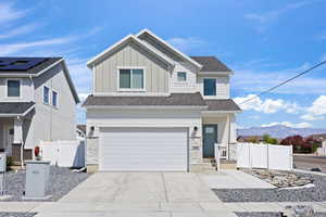 View of front of home with board and batten siding, a gate, a garage, concrete driveway, and stone siding