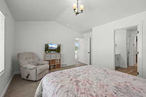 Carpeted bedroom featuring vaulted ceiling, a chandelier, and connected bathroom