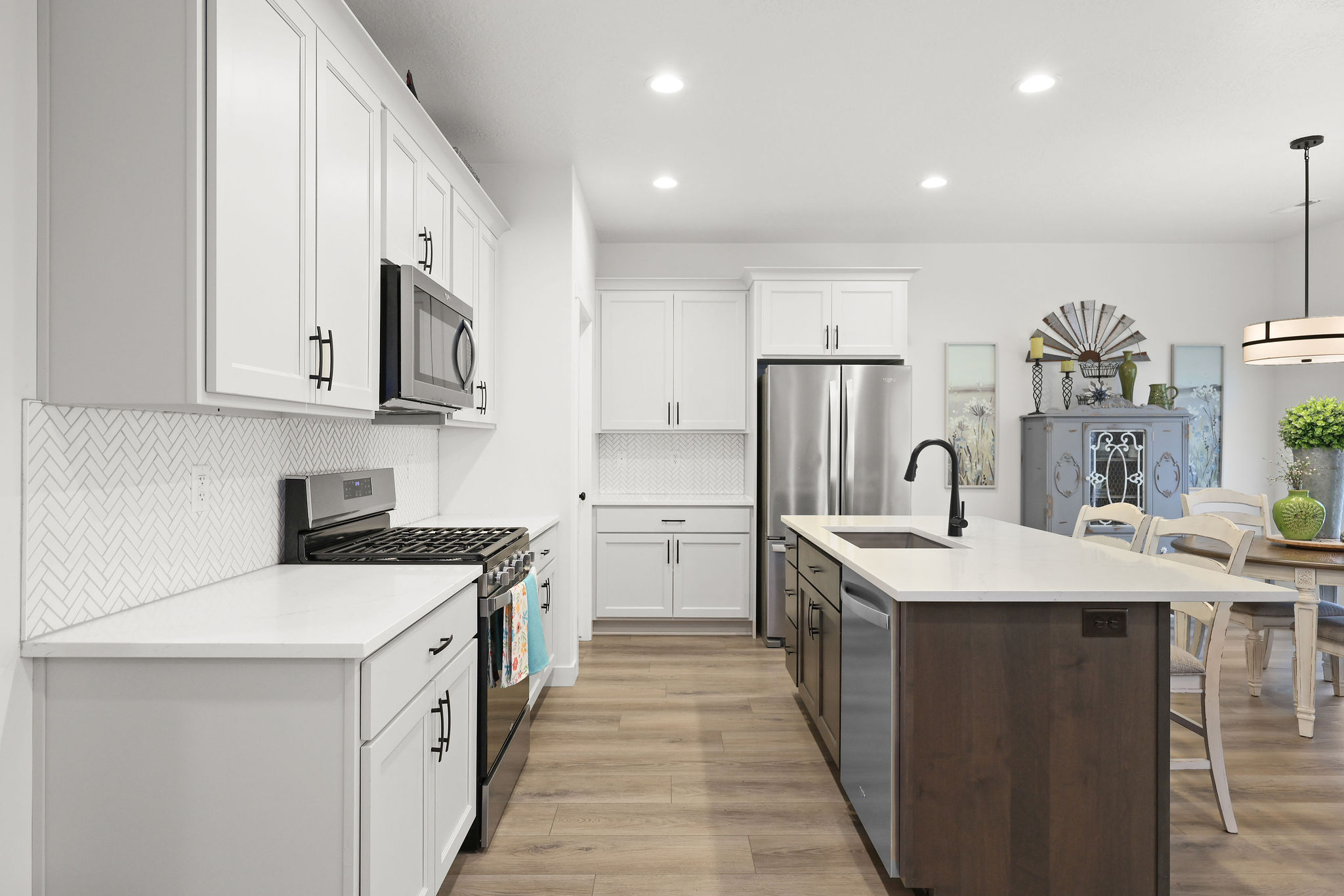 Kitchen featuring two tone cabinets, stainless steel appliances, a breakfast bar, decorative light fixtures, and a center island with sink