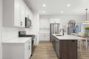 Kitchen featuring two tone cabinets, stainless steel appliances, a breakfast bar, decorative light fixtures, and a center island with sink