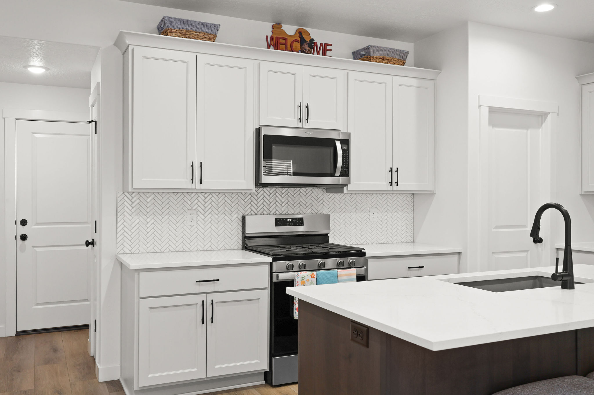 Two tone kitchen featuring stainless steel appliances, tasteful backsplash, light wood-style floors, dual tone cabinets, and light stone countertops