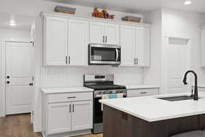 Two tone kitchen featuring stainless steel appliances, tasteful backsplash, light wood-style floors, dual tone cabinets, and light stone countertops