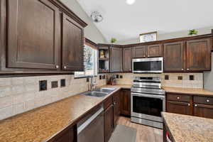 Kitchen with dark wood finish cabinetry, stainless steel appliances, lofted ceiling, light countertops, and decorative backsplash