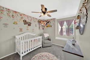 Bedroom with a crib, light carpet, and ceiling fan