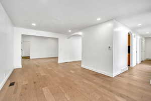 Unfurnished room featuring arched walkways, light wood-style flooring, and recessed lighting