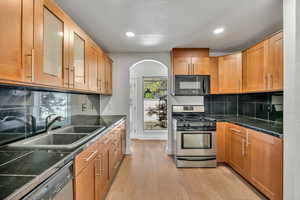 Kitchen featuring dark countertops, stainless steel appliances, recessed lighting, light wood-style floors, and glass insert cabinets