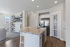Kitchen with a breakfast bar area, white cabinetry, stainless steel appliances, dark wood finished floors, and a textured ceiling