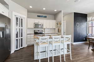 Kitchen with white cabinetry, a center island with sink, stainless steel appliances, a breakfast bar area, and a textured ceiling