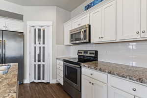 Kitchen with stainless steel appliances, white cabinetry, dark wood-type flooring, and backsplash