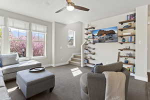 Carpeted living area with ceiling fan and stairway
