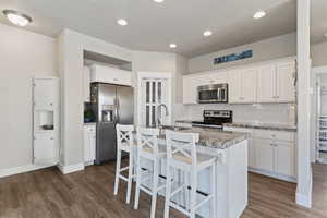 Kitchen with white cabinetry, stainless steel appliances, an island with sink, a breakfast bar area, and tasteful backsplash