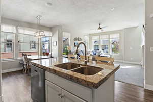 Kitchen featuring open floor plan, light stone counters, a center island with sink, ceiling fan, and stainless steel dishwasher