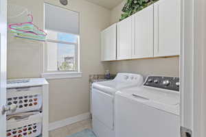 Laundry area featuring cabinet space, light tile patterned flooring, and independent washer and dryer