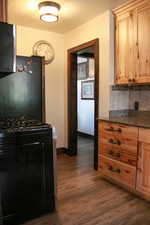 Kitchen featuring black range with gas cooktop, freestanding refrigerator, dark stone countertops, dark wood-type flooring, and decorative backsplash