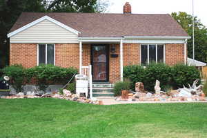 Ranch-style home featuring a front yard, brick siding, a chimney, and roof with shingles