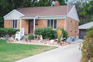 View of front of property featuring brick siding, a front lawn, an outdoor structure, and a shingled roof