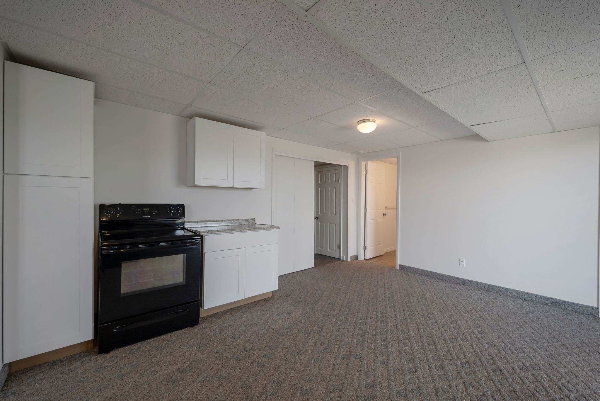 Kitchen with black range with electric stovetop, white cabinetry, a paneled ceiling, dark carpet, and light stone countertops
