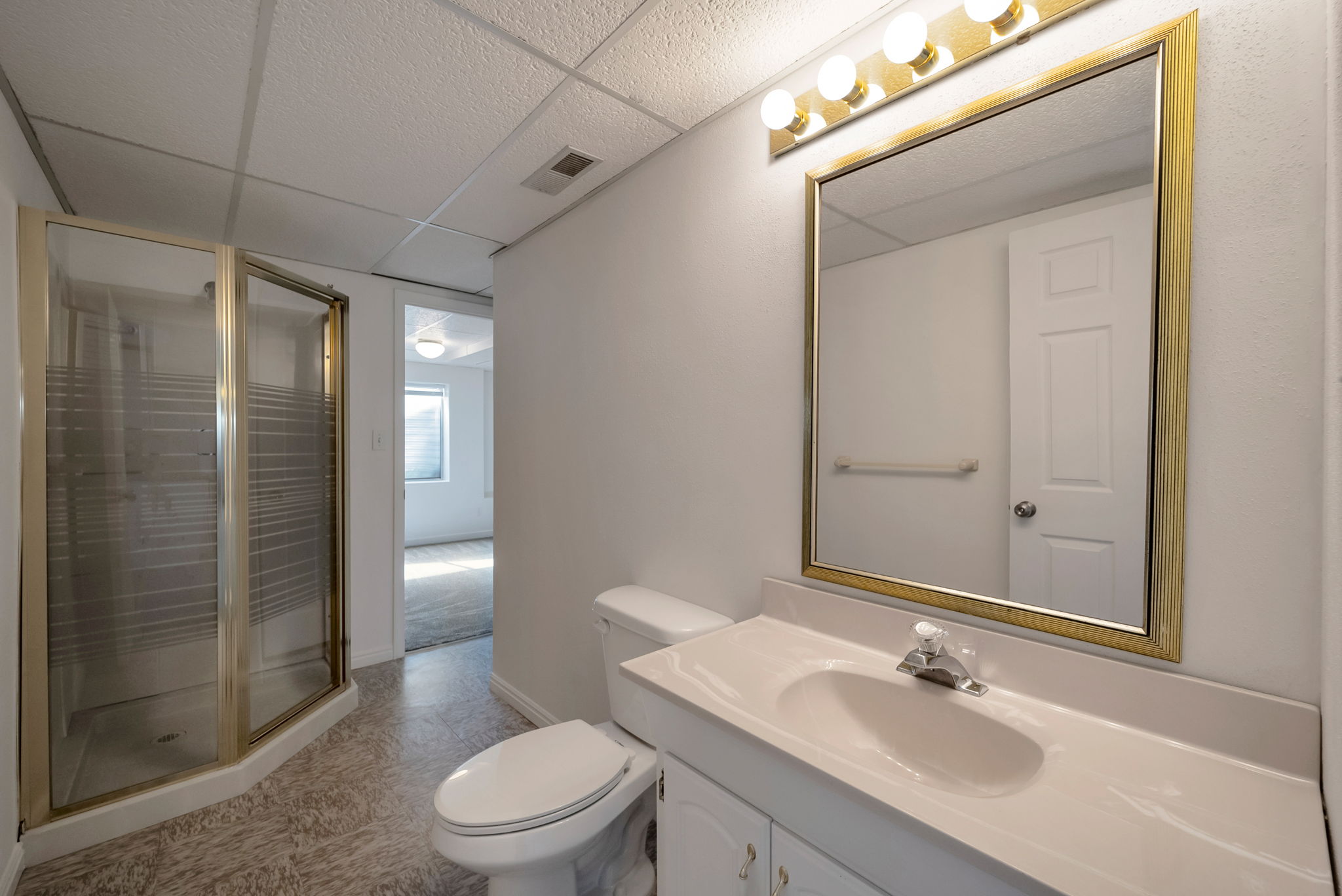 Full bath featuring a drop ceiling, vanity, a stall shower, and light floors