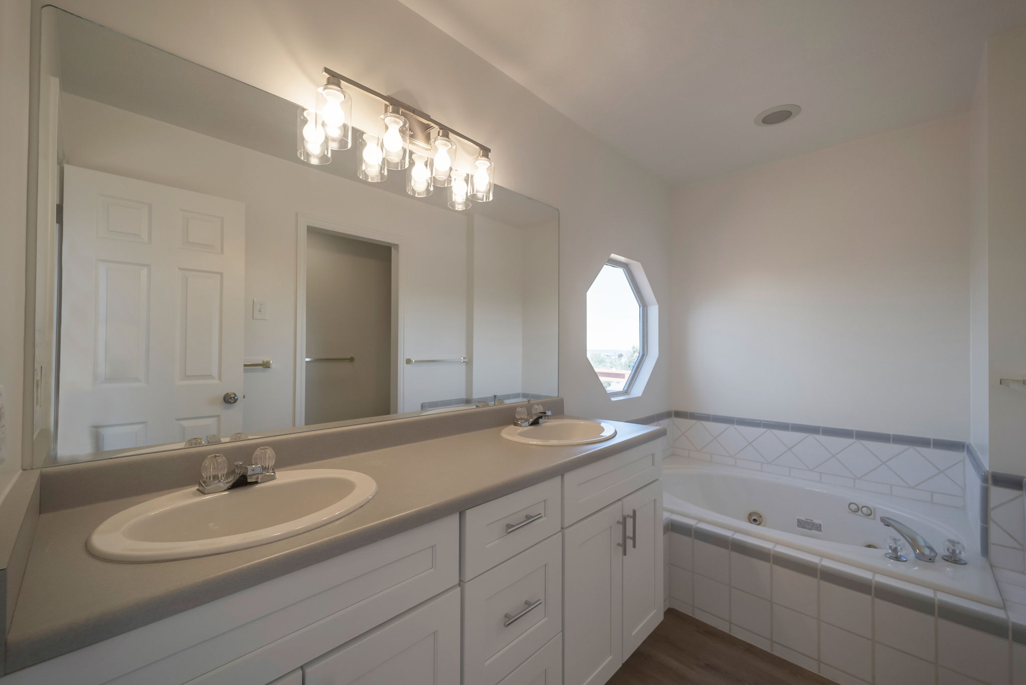 Full bath with double vanity, dark wood-type flooring, and a jetted tub
