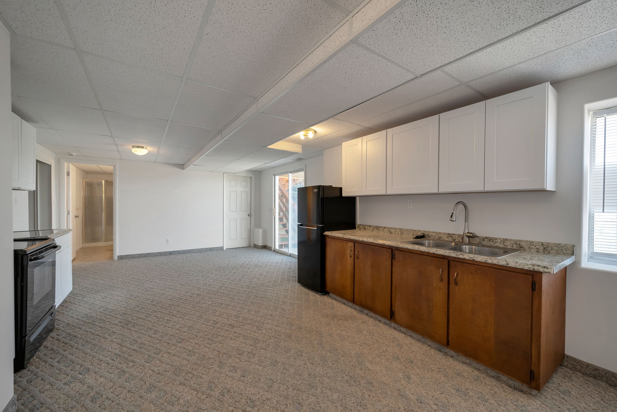 Dual tone kitchen featuring a paneled ceiling, light colored carpet, black appliances, and two tone cabinetry