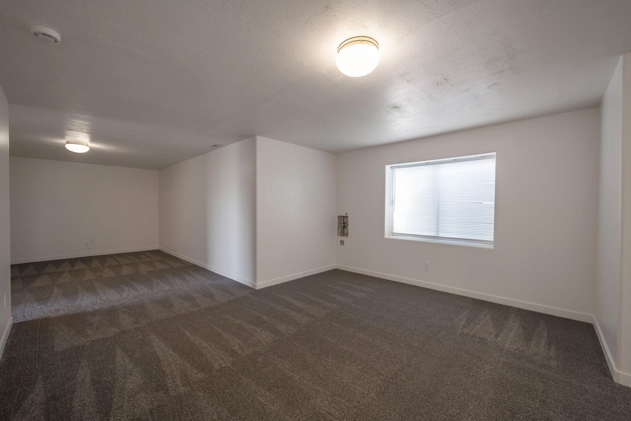 Empty room with dark colored carpet and a smoke detector