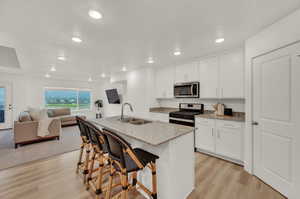 Kitchen with light stone counters, gas range, light wood finished floors, a kitchen bar, and open floor plan