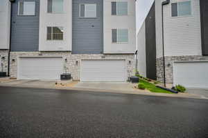 View of front facade featuring stone siding, a garage, stucco siding, and driveway
