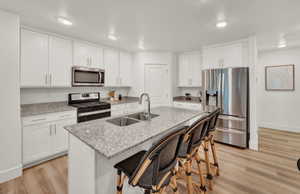 Kitchen featuring light stone countertops, stainless steel appliances, light wood finished floors, a breakfast bar, and white cabinets