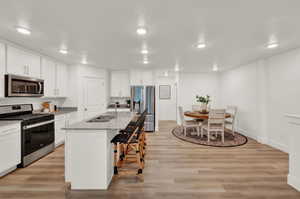 Kitchen featuring stainless steel appliances, light stone countertops, white cabinets, light wood-type flooring, and recessed lighting
