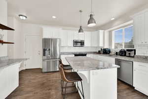 Kitchen featuring light stone countertops, stainless steel appliances, a breakfast bar area, and white cabinets