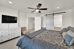 Bedroom with light colored carpet, ceiling fan, a barn door, recessed lighting, and ensuite bath