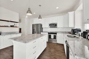 Kitchen featuring light stone countertops, stainless steel appliances, white cabinetry, a center island, and dark wood-style flooring