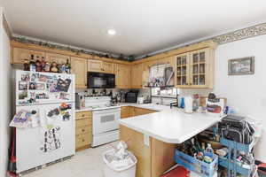 Kitchen with white appliances, glass fronted cabinets, a peninsula, light countertops, and light wood finish cabinets