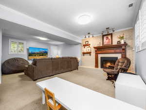 Living area featuring carpet, brick wall, a brick fireplace, crown molding, and a textured ceiling