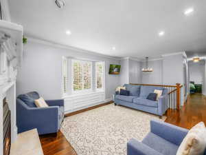 Living room with ornamental molding, dark wood-style floors, a lit fireplace, and recessed lighting