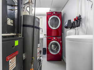 Laundry room featuring strapped water heater, heating unit, stacked washer and clothes dryer, concrete flooring, and a paneled ceiling