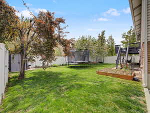 Fenced backyard featuring a trampoline, a vegetable garden, and a deck