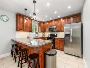 Kitchen featuring a breakfast bar area, stainless steel appliances, a peninsula, tasteful backsplash, and wood finish cabinets