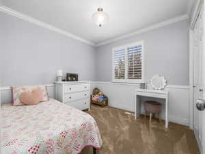 Bedroom featuring wainscoting, crown molding, dark carpet, and a closet