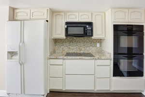 Kitchen with black appliances, cream cabinetry, light stone counters, and dark wood-type flooring