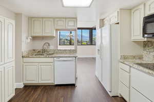 Kitchen with white appliances, light stone countertops, dark wood-type flooring, cream cabinetry, and a mountain view